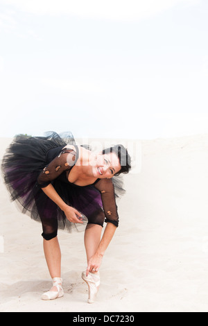 A ballerina in a tutu and pointe shoes on the desert sand leans over to stretch, lots of space for your copy. Stock Photo