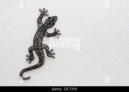 Wire lizard sculpture on a white textured wall. Stock Photo