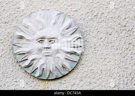 Stylised sun face plaque on a white textured wall. Stock Photo