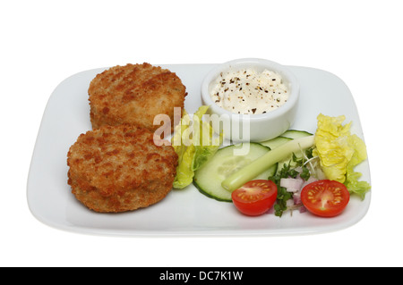 Fishcakes with a salad garnish and a ramekin of mayonnaise on a plate isolated against white Stock Photo