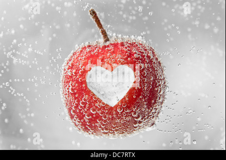 Red Apple with heart-shape cut-out in middle, floating in bubbly water. Stock Photo