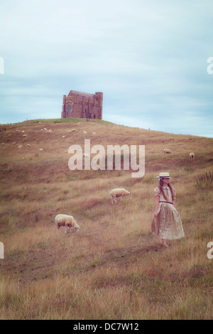 a girl in a vintage dress on a meadow with sheeps, in the background a chapel Stock Photo