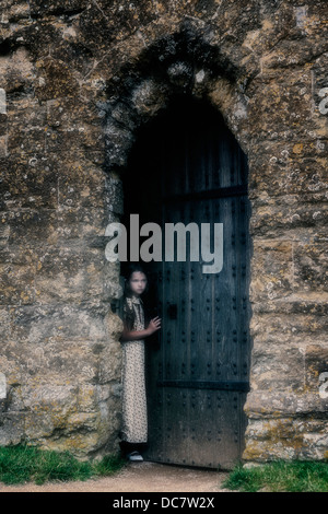 a girl is looking out of an old door Stock Photo