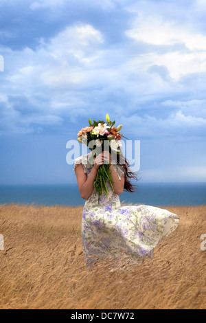 a girl in a floral dress on a field hiding behind a bouquet of flowers Stock Photo