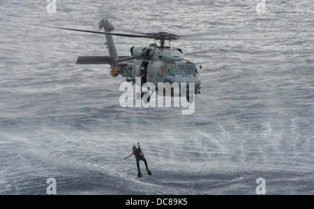 A US Navy search and rescue swimmer prepares to rescue a simulated man overboard during a helicopter cast off and recovery exercise with Arleigh Burke-class guided-missile destroyer USS Preble August 9, 2013 operating in the Pacific Ocean. Stock Photo
