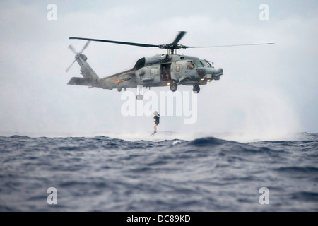 A US Navy search and rescue swimmer jumps into the ocean from an SH-60R Seahawk during a helicopter cast off and recovery exercise with Arleigh Burke-class guided-missile destroyer USS Preble August 9, 2013 operating in the Pacific Ocean. Stock Photo