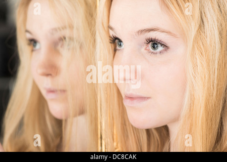 Portrait of young blond female teenager standing by mirror looking sad Stock Photo