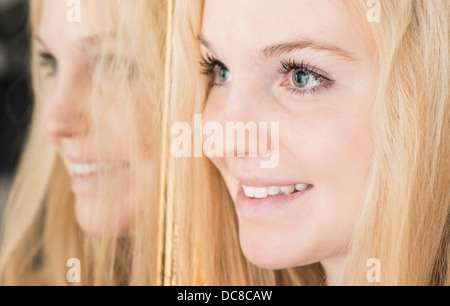 Portrait of happy young blond female teenager standing by mirror looking away