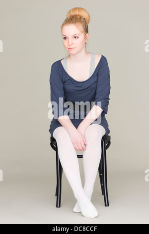 Pensive young blond female teenager in ballet dress sitting on chair Stock Photo