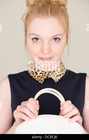 Young blond woman holding white hand bag, looking at camera with nervous expression Stock Photo