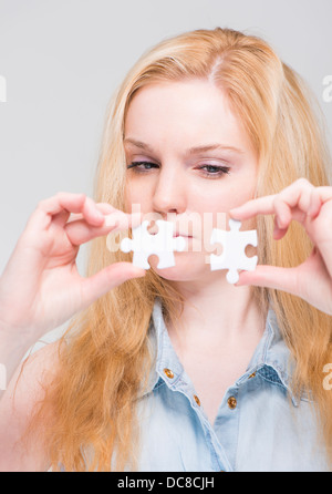 Young blonde woman holding and examining two white puzzle pieces Stock Photo