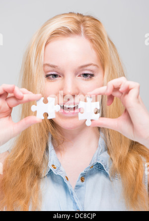Young smiling blonde woman holding and examining two white puzzle pieces Stock Photo