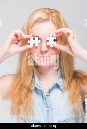 Young blonde woman holding two white puzzle pieces in front of her eyes Stock Photo