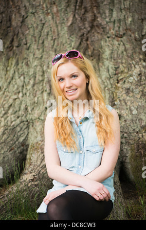 One young blonde attractive woman in front of big tree in a park Stock Photo