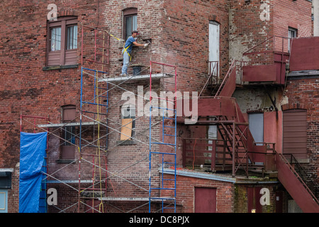 A brick mason works on a scaffolding three stories high to repair a brick wall in St. John, Nova Scotia, Canada. Stock Photo