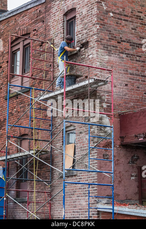 A brick mason works on a scaffolding three stories high to repair a brick wall in St. John, Nova Scotia, Canada. Stock Photo