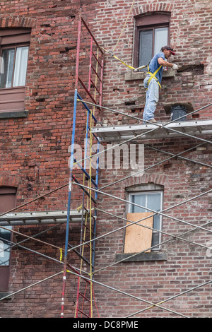 A brick mason works on a scaffolding three stories high to repair a brick wall in St. John, Nova Scotia, Canada. Stock Photo