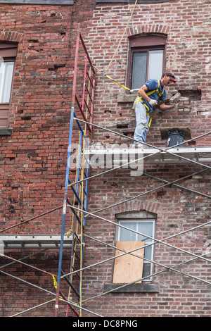 A brick mason works on a scaffolding three stories high to repair a brick wall in St. John, Nova Scotia, Canada. Stock Photo
