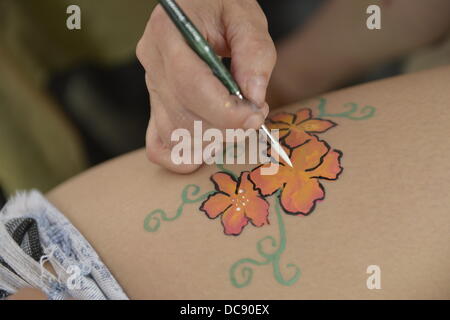 Brooklyn, New York, USA. 10th August 2013.  Closeup of artist hand painting flowers on girl's leg with brush. Stock Photo