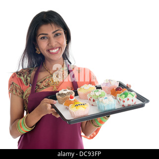 Happy Traditional Indian woman in sari baking bread and cupcakes, wearing apron holding tray isolated on white. Stock Photo