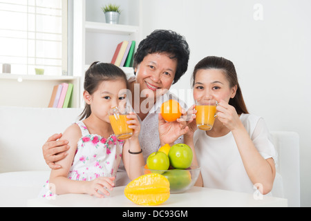 Asian family drinking orange juice. Happy Asian grandparent, parent and grandchild enjoying cup of fresh squeeze fruit juice at home. Stock Photo