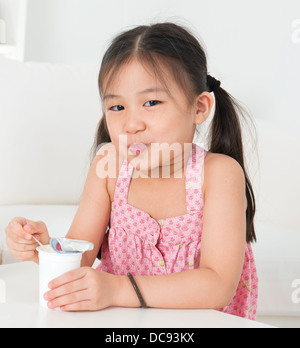 Eating yogurt. Happy Asian kid eating yoghurt at home. Beautiful child. Healthcare concept. Stock Photo