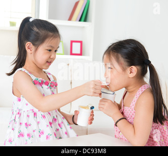 Eating yogurt. Happy Asian children eating yoghurt at home. Beautiful sisters . Healthcare concept. Stock Photo