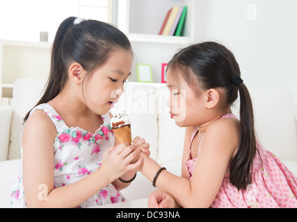 Eating ice cream cone. Asian girls sharing an ice cream. Beautiful children model at home. Stock Photo