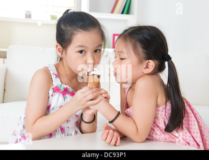 Eating ice cream cone. Asian children sharing an ice cream at home. Beautiful girls model. Stock Photo