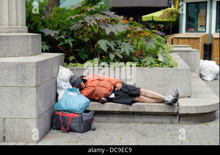 Homeless man sleeping on a concrete bench in downtown Montreal. Stock Photo