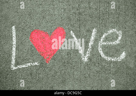 the word love is written in white chalk on a sidewalk, and has a pink heart for the letter o. Stock Photo