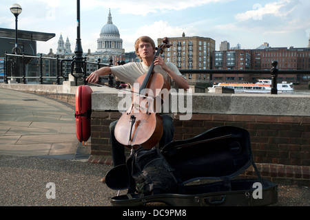 A young man busker playing the classical music on cello with a view of St. Paul's Cathedral Southbank London UK  KATHY DEWITT Stock Photo