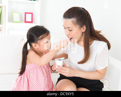 Eating yogurt. Happy Asian family eating yoghurt at home. Beautiful child feeding mother, healthcare concept. Stock Photo