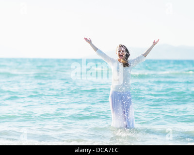 Smiling young woman standing in sea and sprinkling water Stock Photo