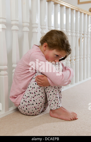 young girl upset sad and lonely holding head in hands crying huddled on landing against balustrade Stock Photo