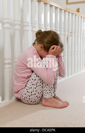 young girl upset sad and lonely holding head in hands crying huddled on landing against balustrade Stock Photo