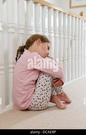 young girl upset sad and lonely holding head in hands crying huddled on landing against balustrade Stock Photo