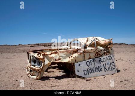 View of a car wreck with numerous bullet holes and a sign 'Off Road Driving Kills' on a never-ending road near Brandberg West north of Swakopmund in Skeleton Coast National Park in Namibia, 6 December 2010. Photo: Tom Schulze Stock Photo