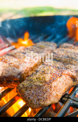 Two beef steaks on cast iron grate grilling over open fire on outdoor barbecue grill Stock Photo