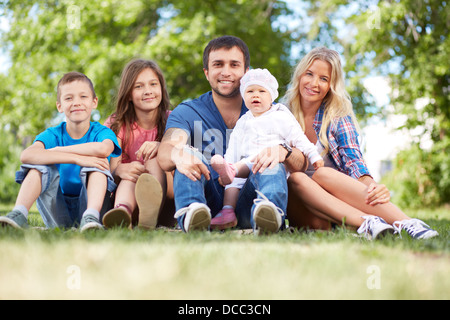 Photo of happy family sitting on grass during summer rest Stock Photo