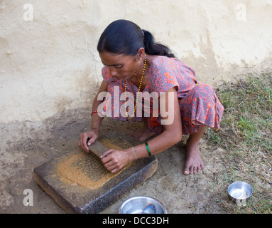 Woman grinding spices and chilli as she is preparing achar (spicy pickle) for a meal in a Tharu village, Nepal Stock Photo