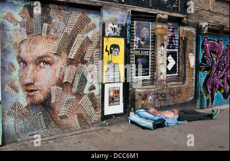 Rough sleeper sleeping next to street art in the Brick Lane district of East London United Kingdom Stock Photo