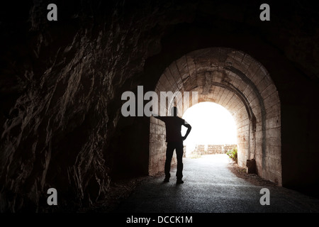 Young man stands relaxed in dark tunnel and looks in the light