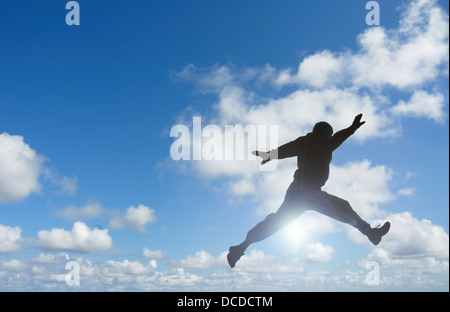 Silhouette of man jumping set against blue sky and clouds. Stock Photo