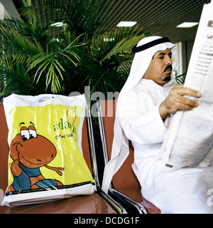 Reading his newspaper to pass the time, a businessman in traditional Gulf state thawb and agal headdress awaits his flight from Bahrain in the Persian Gulf. Stock Photo