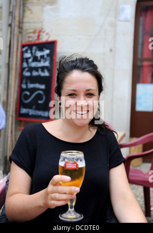 Young woman 20s drinking a glass of Stella Artois beer lager outside a bar at Puy L'Eveque in the Lot Region France Stock Photo