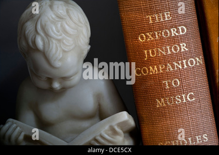 MUSIC STUDY BOOKS Bookend statue of young boy reading alongside classical music book in library Stock Photo