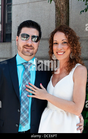 groom wearing sunglasses & his pretty red haired bride pose on Lower Manhattan sidewalk after City Hall wedding New York City Stock Photo