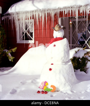 melting snowman stands in yard of cottage with melting icicles on snowy roof in shasta calif Stock Photo