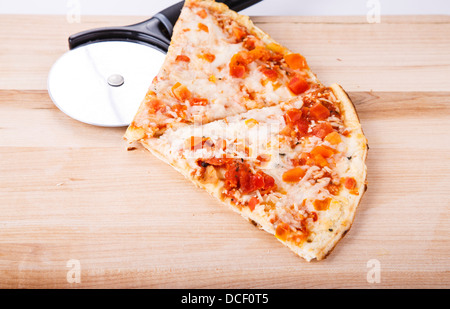 Slices of tomato pizza on a wood cutting board with pizza cutting whell Stock Photo